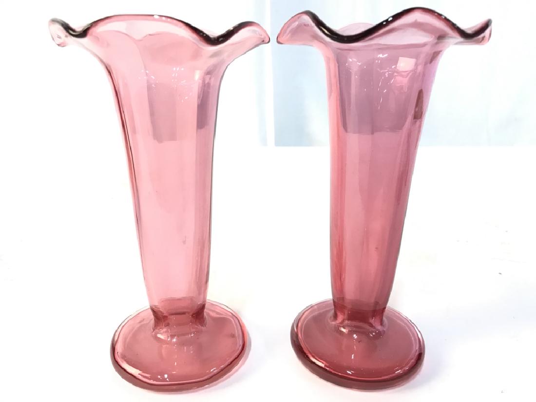 Pair Cranberry Glass Vases: Vases have magenta cranberry tone. Rim has furled detail. Piece is footed. Measures approx 7 inches tall 4 inches wide. decor piece, art glass decor, home accent, home accessory, tableware, shelf piec