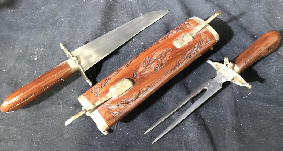 Carved Wooden Knives w Carved Wooden Holster: Lot includes 1 two pronged forked knife, 1 holster, & 1 knife with carved wooden handle. Each knife has carved wooden handle. Holster has carved wooden detail. Measures approx 17 inches long when put 