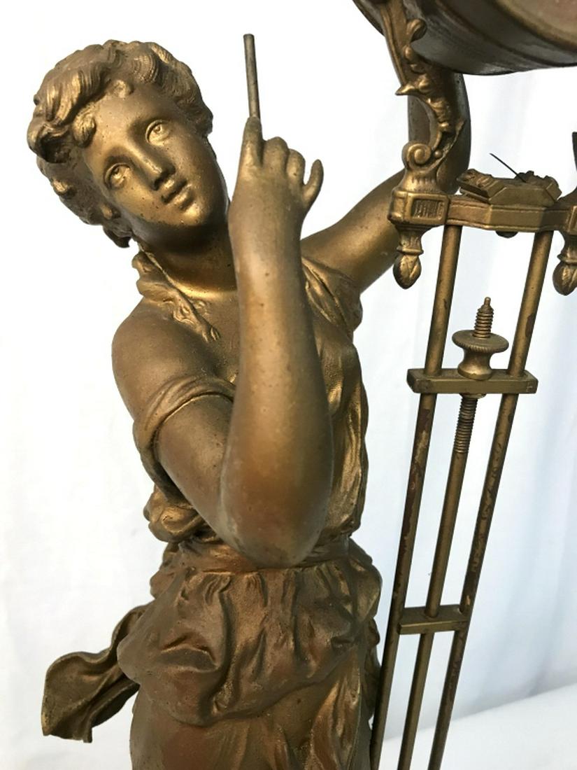 Brass Toned Female Figural Clock: Piece is brass toned. Contains black toned circular base. Piece has female Figural structure holding a clock. Piece is vintage. Piece measures approx 25 inches tall 7 inches wide. Female figure, woman