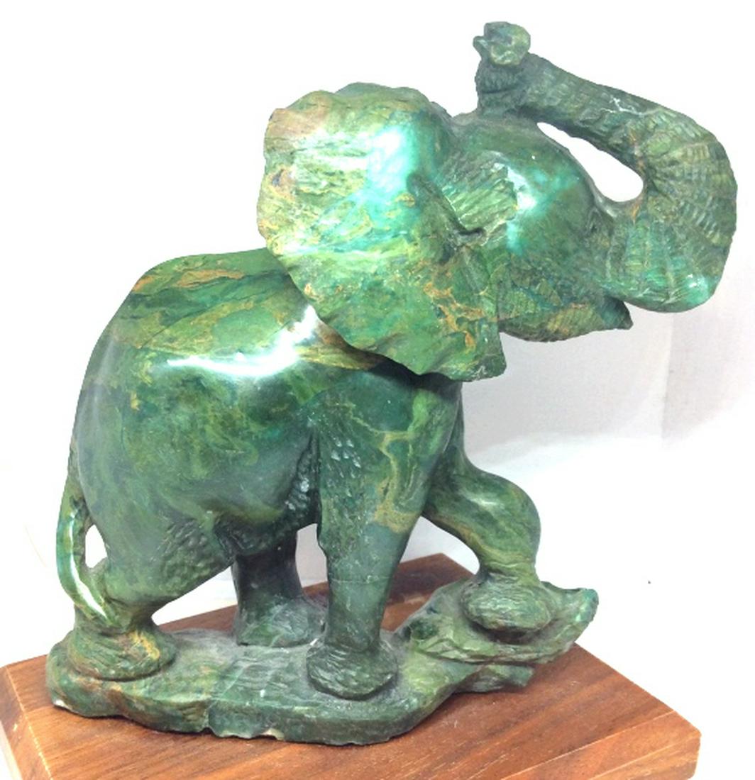 Malachite Carved Elephant: Green toned natural Stone / Malachite. Carved elephant, mounted on wood base. Measures approx 8 in by 6in by 5 in. Some minor surface wear, appears to have once had tusks. Decorative arts and accessor