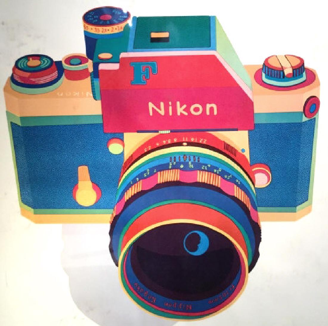 Framed Anne Laddon Nikon Poster Print: Poster print depicts a colorful Nikon camera illustration with type ‘Anne Laddon, Sure Shot’ along top. Poster is set behind plastic. Measures approx 30.2 inches in height by 24.25 inches in width