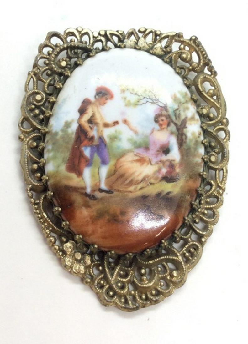 Porcelain plaque Pendant: Brass toned metal pendant with openwork filigree designs, oval porcelain plaque with romantic scene of Victorian esque couple in wooded park scene. Measures approx 2 1/2 in by 1 1/2 in, women’s vint