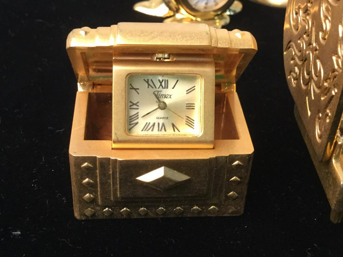 Lot 9 Tabletop Brass Toned Clock Figurines: Timex, Quartz, Azur, BULOVA. in Shapes Of piano, golf ball, snowman, treasure box, present, vanity, pendulum clock, grandfather clock. All possibly need new batteries. Possibly brass. Largest approx 4