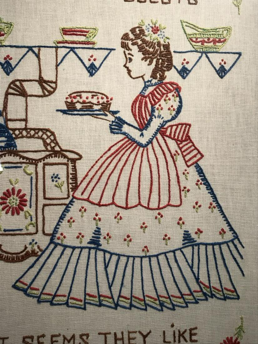 Vintage Motto Sampler W Kitchen Motif: Sampler features the saying ‘no matter where i serve my guests / it seems they like my kitchen best.’ Embroidered woman in dress in kitchen motif. Sampler is set behind glass in wood frame. Sample