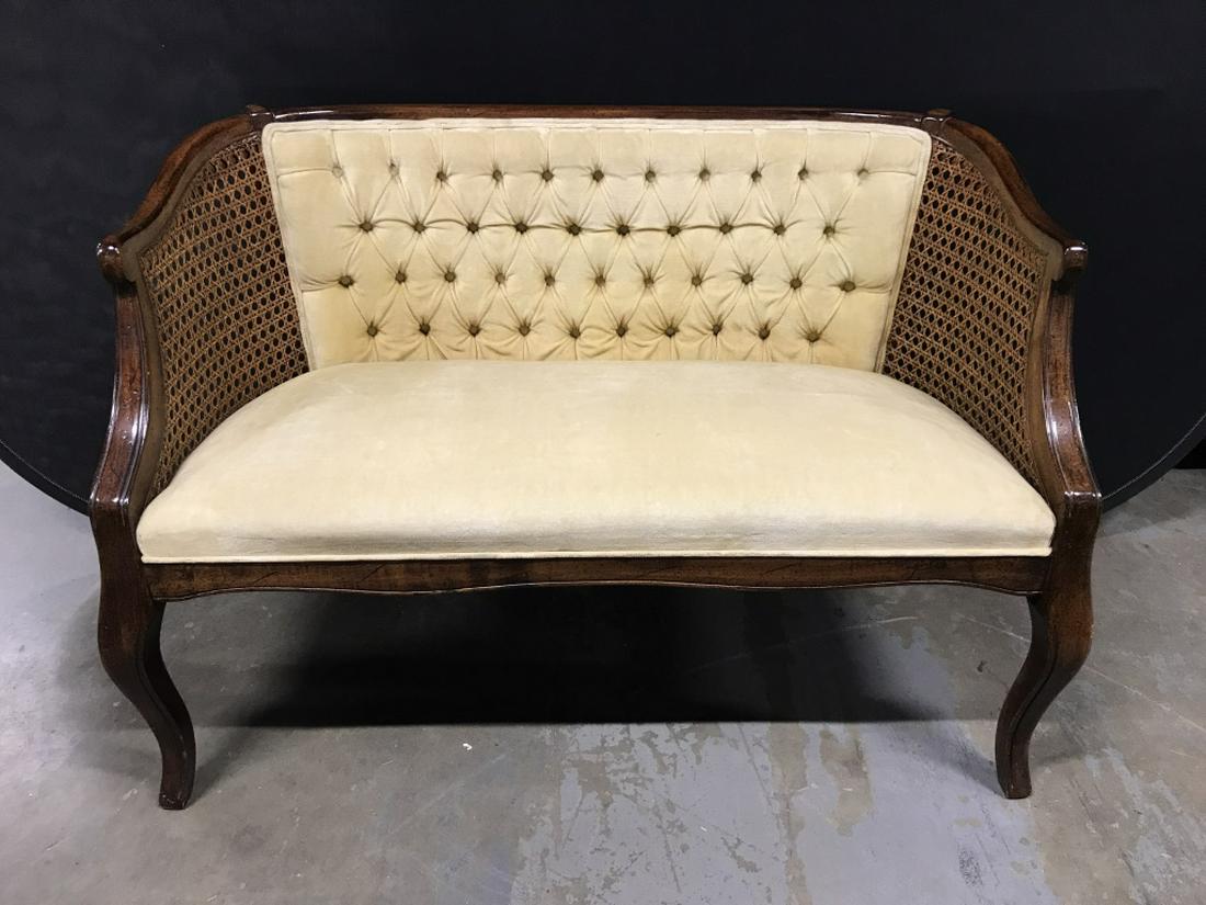 Vintage Tufted Velvet and Cane Woven Settee: Vintage tufted cream tone velvet and cane woven settee. Possibly walnut wood frame. Settee features a curved frame with woven cane side panels and tapered legs. Measures approx 29.75 inches in height 