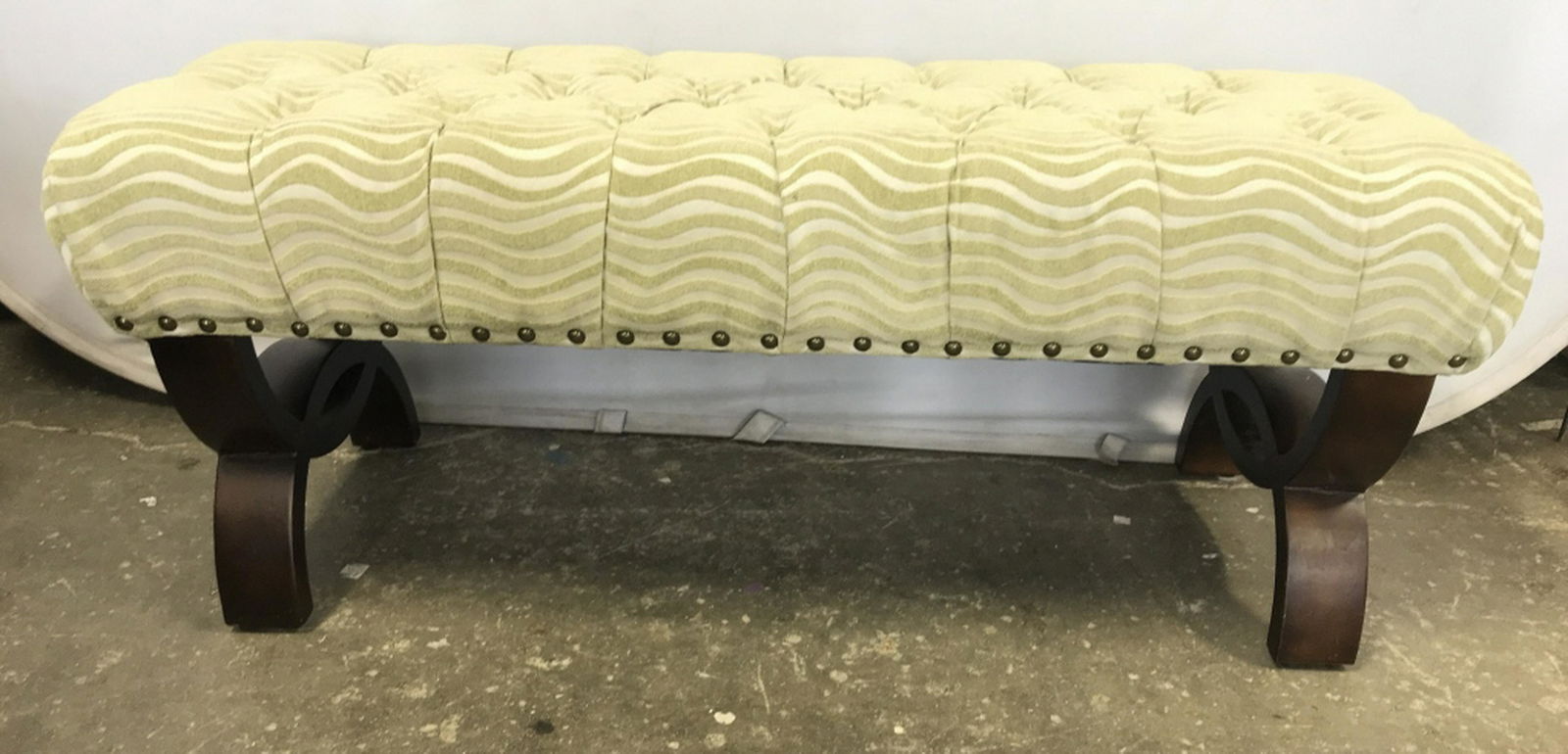 Green Toned Tufted Upholstered Bench: Bench has a light green tone. Contains gold toned studded detail. Piece has wave like pattern. Piece has brown toned supports. Piece measures approx 48 inches long 21 inches tall 18 inches deep. bench