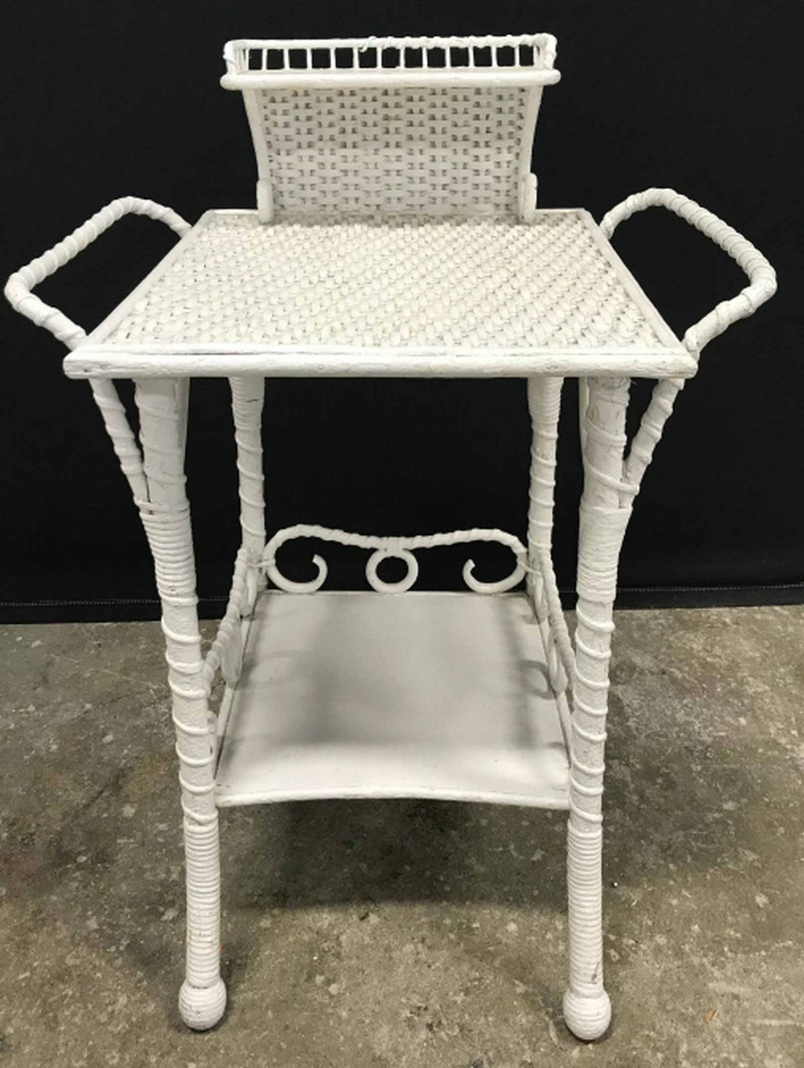 Vintage Wicker Side Table: Vintage Side Table, night stand is painted white in tone. Has Top Gallery and Side handles. Measures approx 27.5 inches in height by 18.25 inches in width by 15 inches in depth. table has surface wear