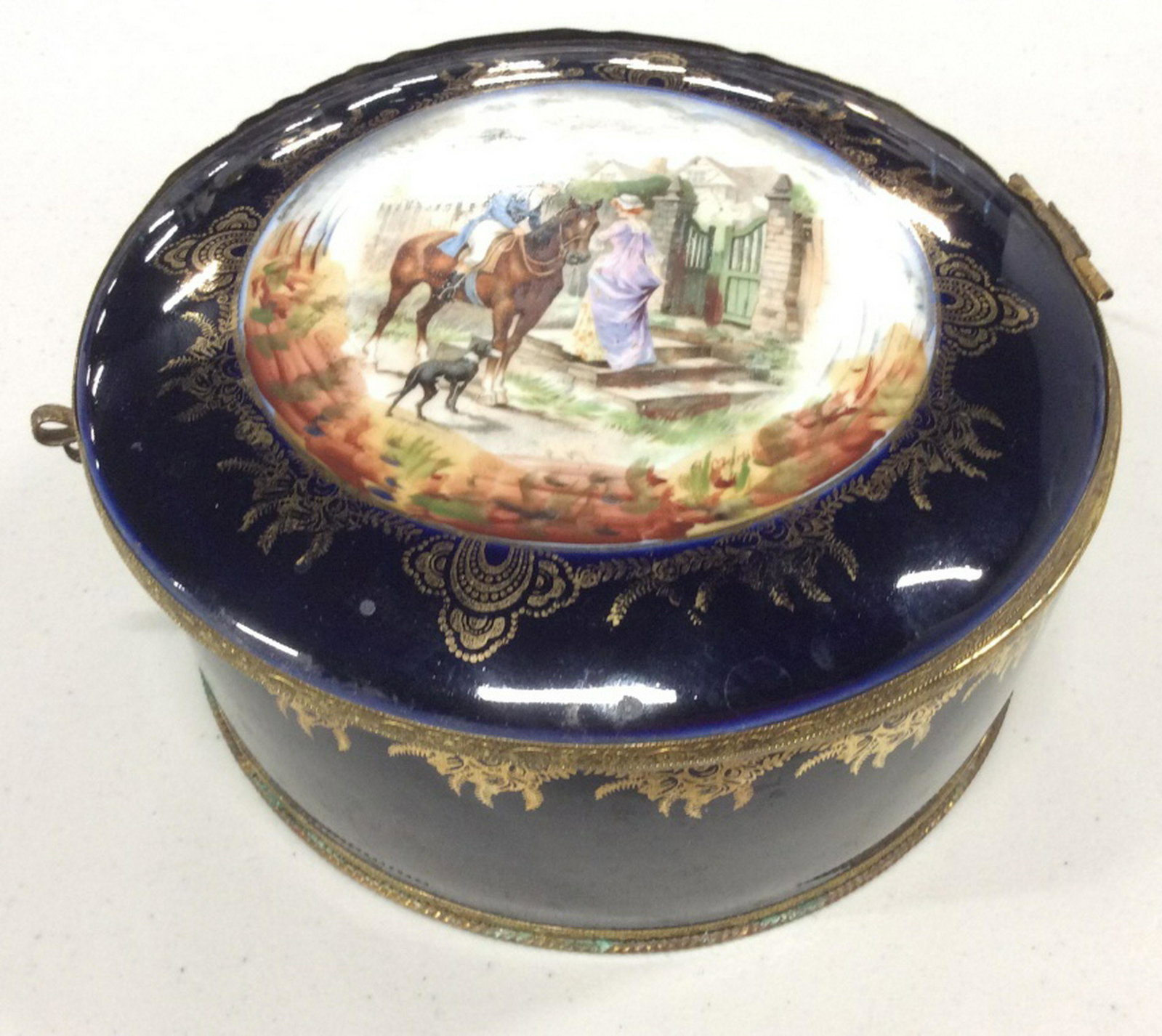 Porcelain Lidded Keepsake Box, Germany: Vintage Porcelain Keepsake Box with Mirror in Underside Lid. Center Picture Medallion in Middle. Gold Tone Trimming. Mirror has a missing piece, some discoloration to metal and other surface wear. Hei