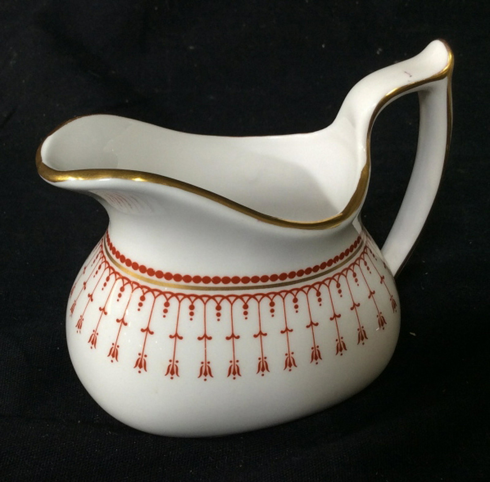 Bone China Cream Pitcher Small Bone China creamer jug.: Small Bone China creamer jug. produced in England by Spode. Stands at approximately 4 inches tall. Painted gold accents on edges with a red design. Creamer jar, creamer jug, small jug, small creamer j