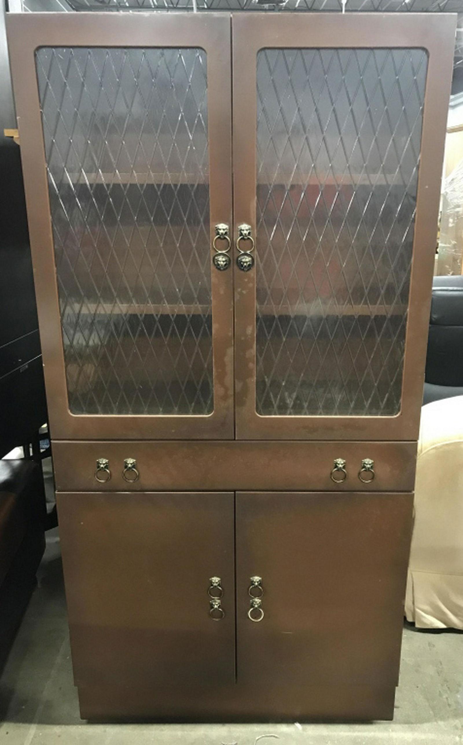 Vintage Chocolate Toned Metal Display Case Display Case: Display Case has a chocolate tone. Top of piece has 2 shelves and doors with diamond shaped relief detail. Center contains 1 Drawer with 4 handles. Lower half has 2 Cabinet doors. Piece measures appro