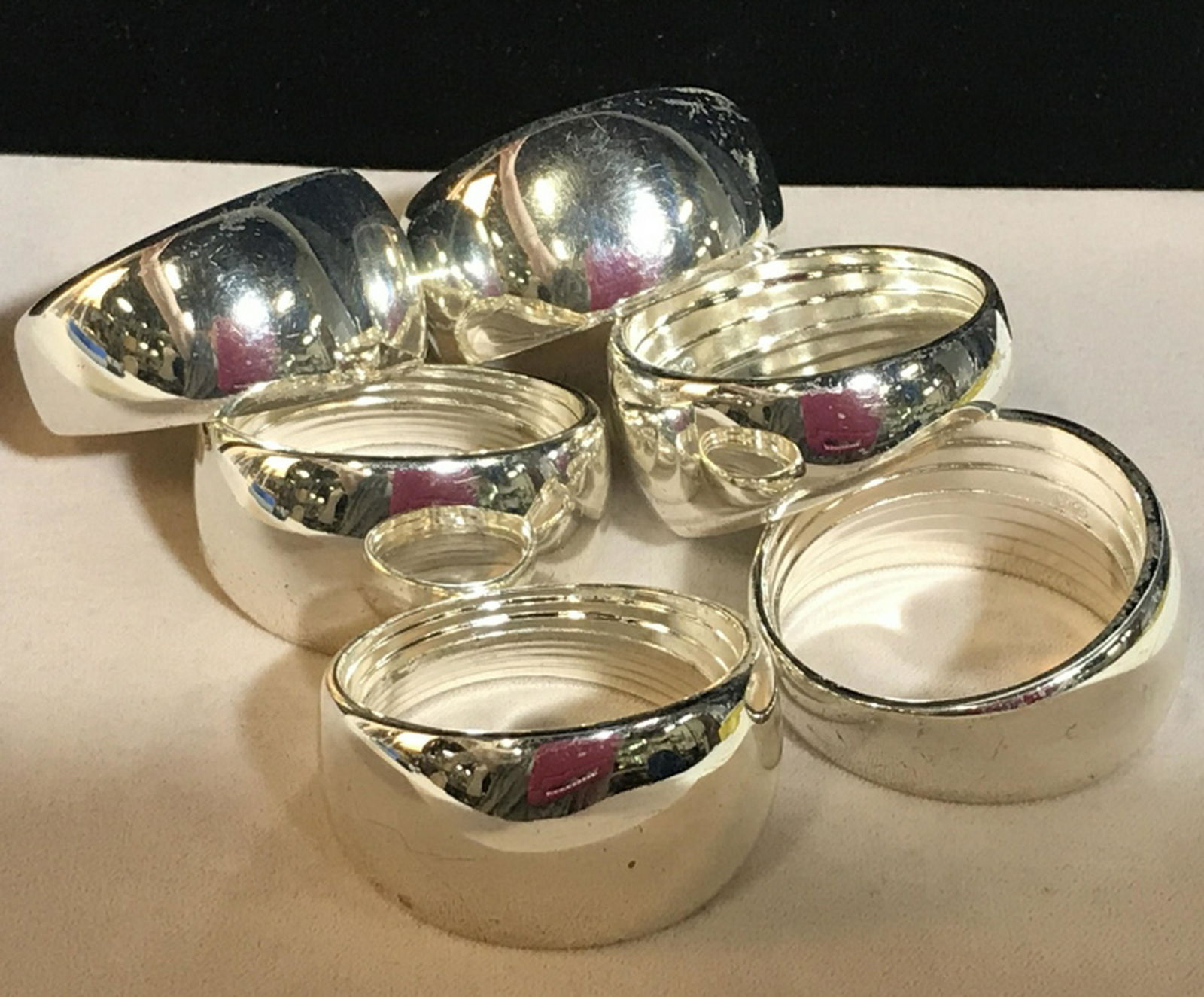 Set 6 Silver Toned Napkin Rings Simple rounded: Simple rounded silhouette with bright shine. Has hallmark in center on interior, appears to be JL with a crown hallmark. Surface scratches are evident, possibly polish to tone down. Wide opening for f