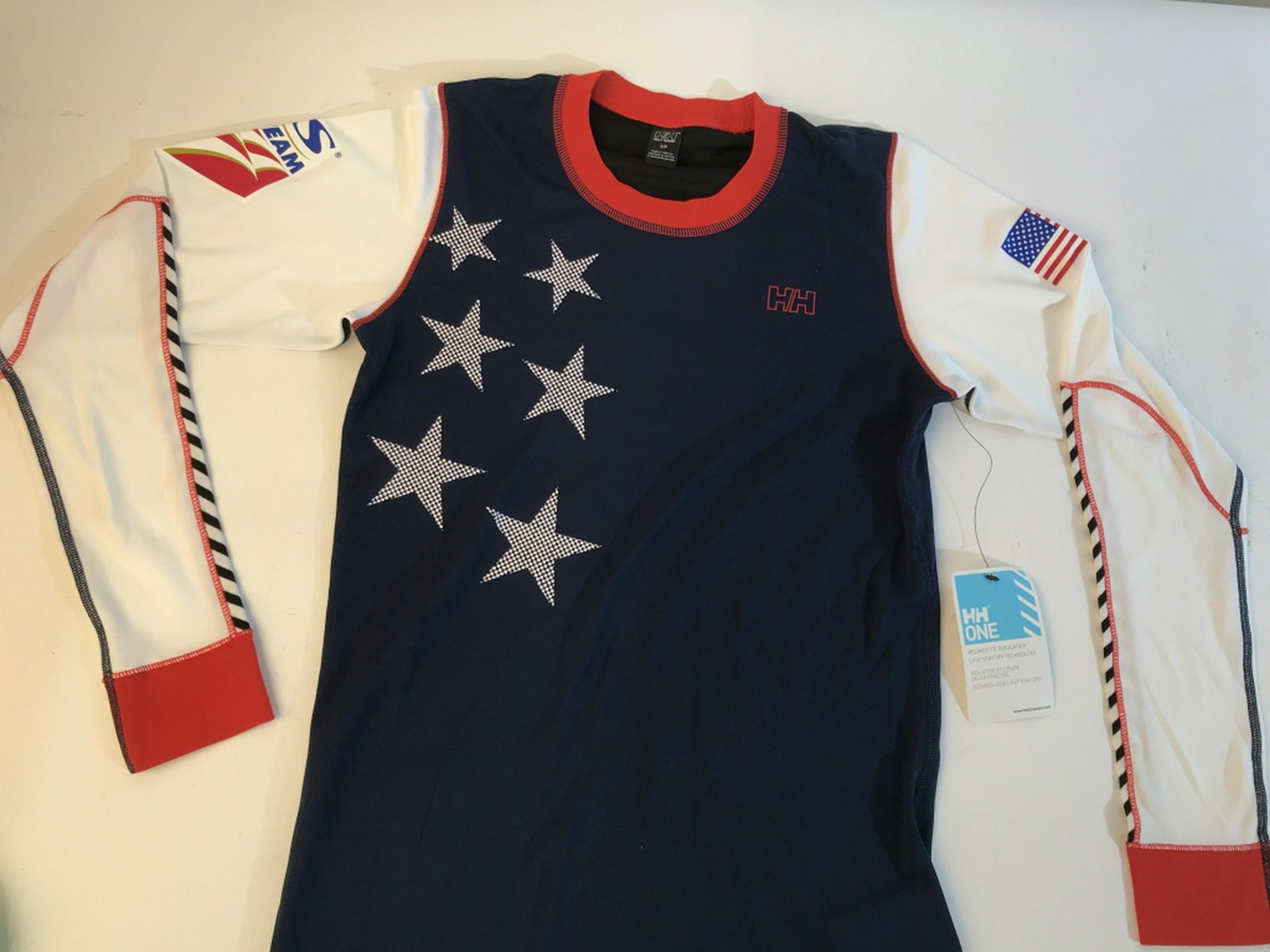 HELLY HANSEN SMALL relaxed fit insulation shirt helly: helly hansen small insulated long sleeve relax fit shirt. In navy blue. Tag still on. Shirt features US Ski Team graphic on right shoulder and American flag on the left. HELLY Hansen logo on the front