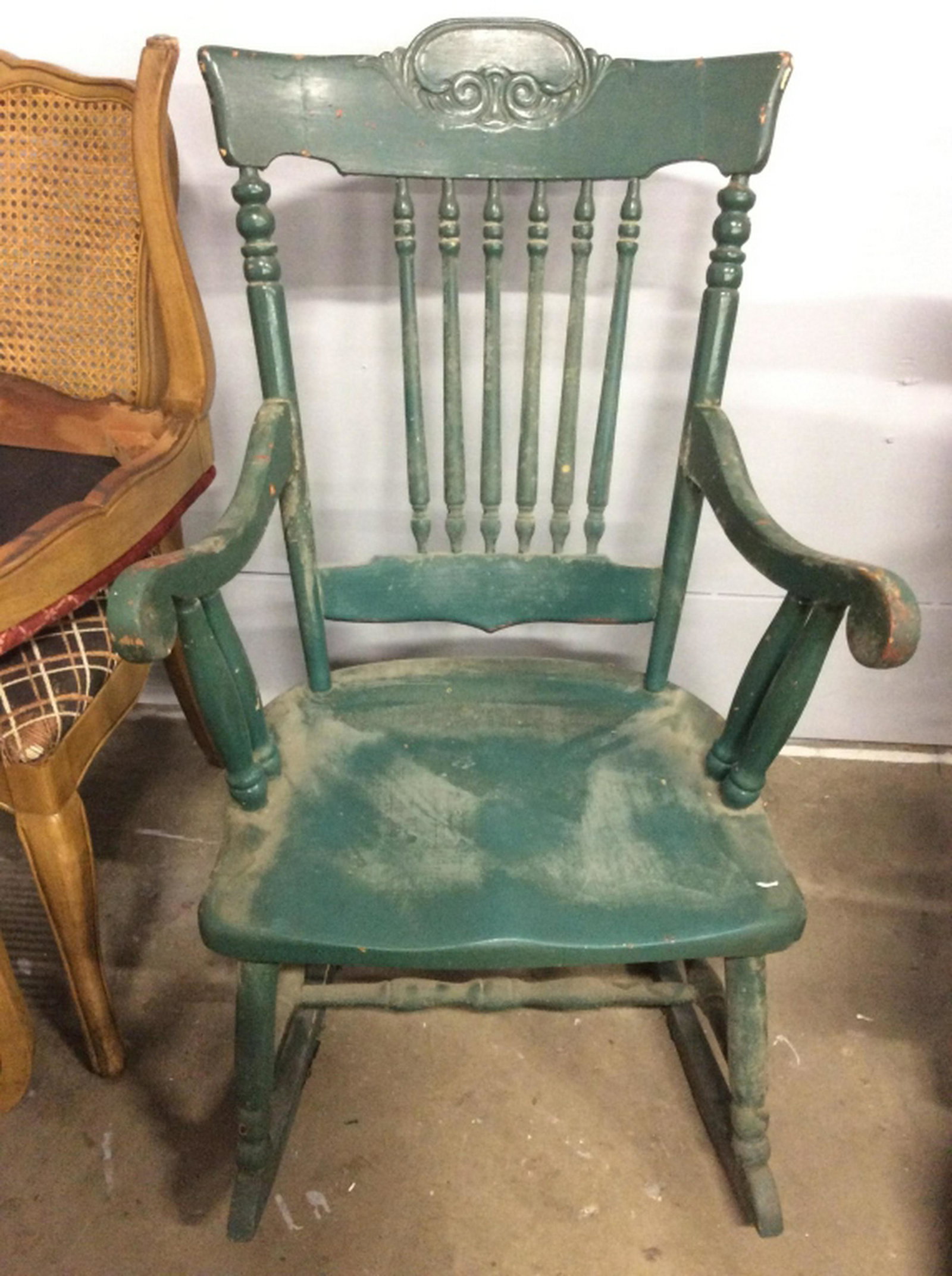 Vintage Carved Wooden Rocking Chair Rocking chair is: Rocking chair is green toned. Piece contains carved wooden detail. Backrest has Spindle style. Piece is vintage. Piece measures approx 38 inches tall 23 inches wide 32 inches deep. Contains some wear,