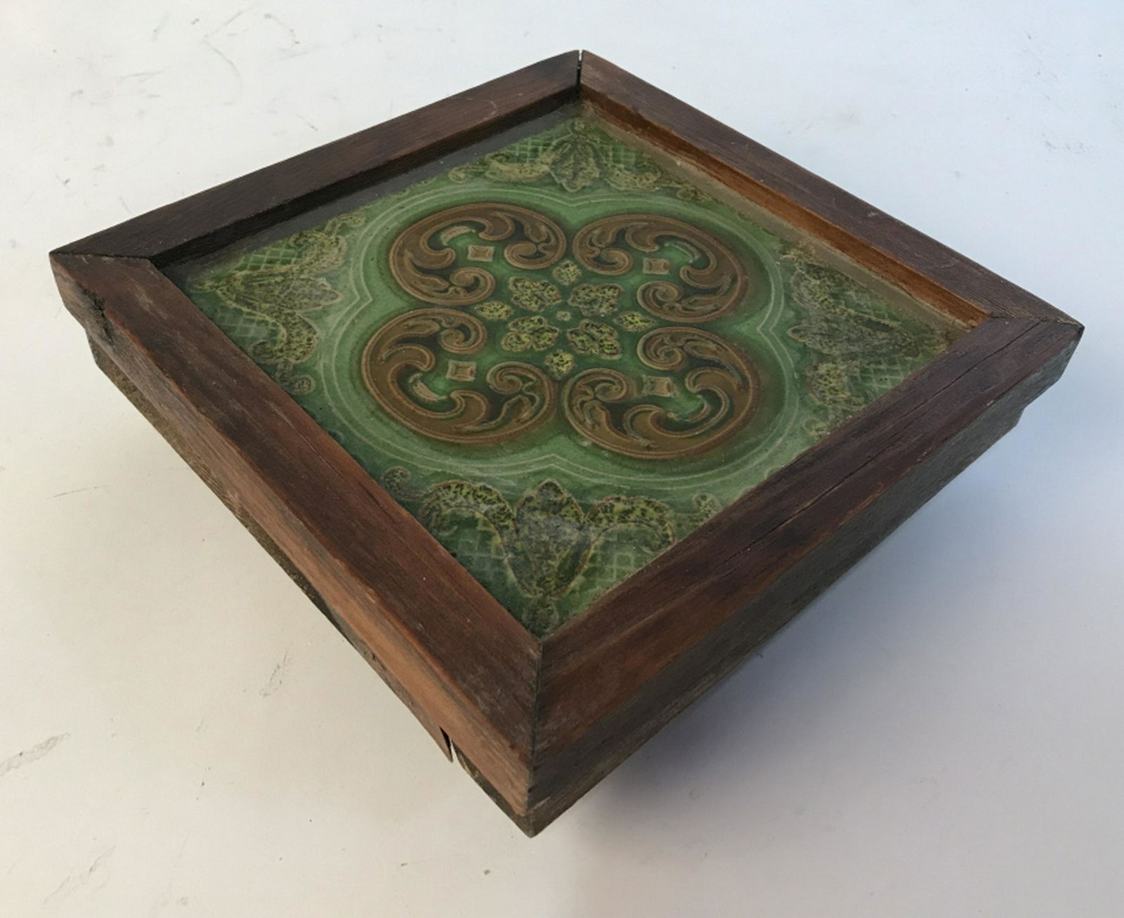 Ceramic on trivet Wooden border. Has wooden feet. Green: Wooden border. Has wooden feet. Green and brown porcelain in the middle. Measures approximately 7.5 inches in length and width and 2.5 inches in height. Wood is dark in color Trivet, vintage trivet, p
