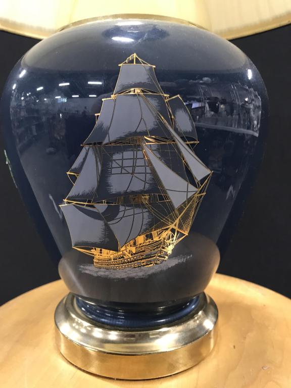 SAILOR SHIP Design Vessel Lamp with Shade: Shape in tulip style with bright gold toned base. Finial top attached to light harp. Height approx 21.5 in. Vessel body circumference 25 in. Pleated cream shade with blue bottom and top rims. Shade 42