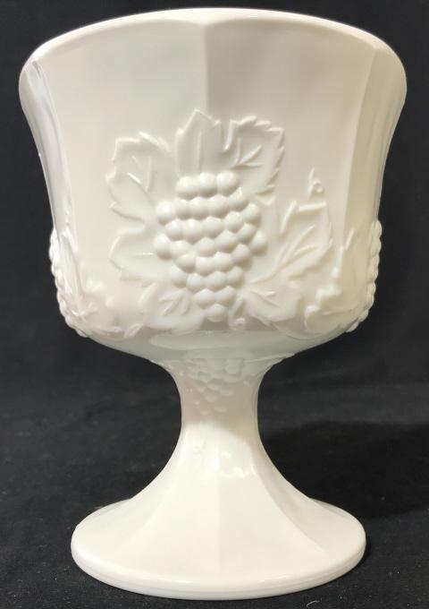 Milk Glass Chalice W Berry & Vine Motif: Milk glass chalice, footed bowl, goblet with berry and vine motif pattern in relief. Measures approx 6.5 inches in height by 5.5 inches in diameter. Underside has paper with handwriting, reads ‘Rive