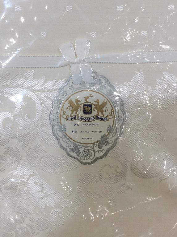 Set Fine Imported Dmask Starlight Table Linens: Wrapped. 13 Total pieces. Cream color Tablecloth and napkin set, made of combed yarn. label reads Fine Imported DMASK Starlight ABADI 51% cotton, 49% rayon. Made in Japan. Tablecloth 64 in x 122 in. N