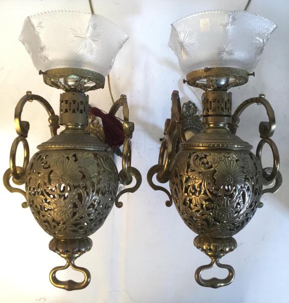 Pair Vintage Gold Toned Brass Wall Lamps: Lot includes 2 wall lamps. Each are gold toned and appear to be brass. Both have intricate pierced floral and leaf detail with c and s curve detail. Each include glass fixture. Each measures approx 18