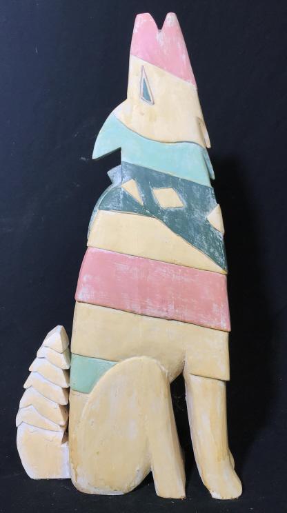 Folk Art Carved Wood Howling Coyote: Southwestern folk art geometrically Carved wooden floor sculpture of howling coyote, wolf. Carved initials along bottom, possibly reads ‘DL.’ Painted in pastel hues of yellow, pink, and turquoise,
