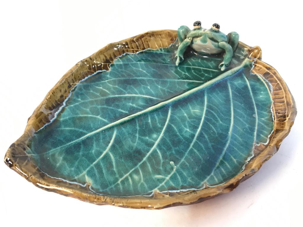 Pair Ceramic Frog On Leaf Trinket Dishes: Lot includes 2 ceramic dishes. Each depicts a frog sitting on a leaf. Each piece has tones of green and light brown. Each measures approx 8 inches long 6 inches wide. handcrafted, whimsical design, tr