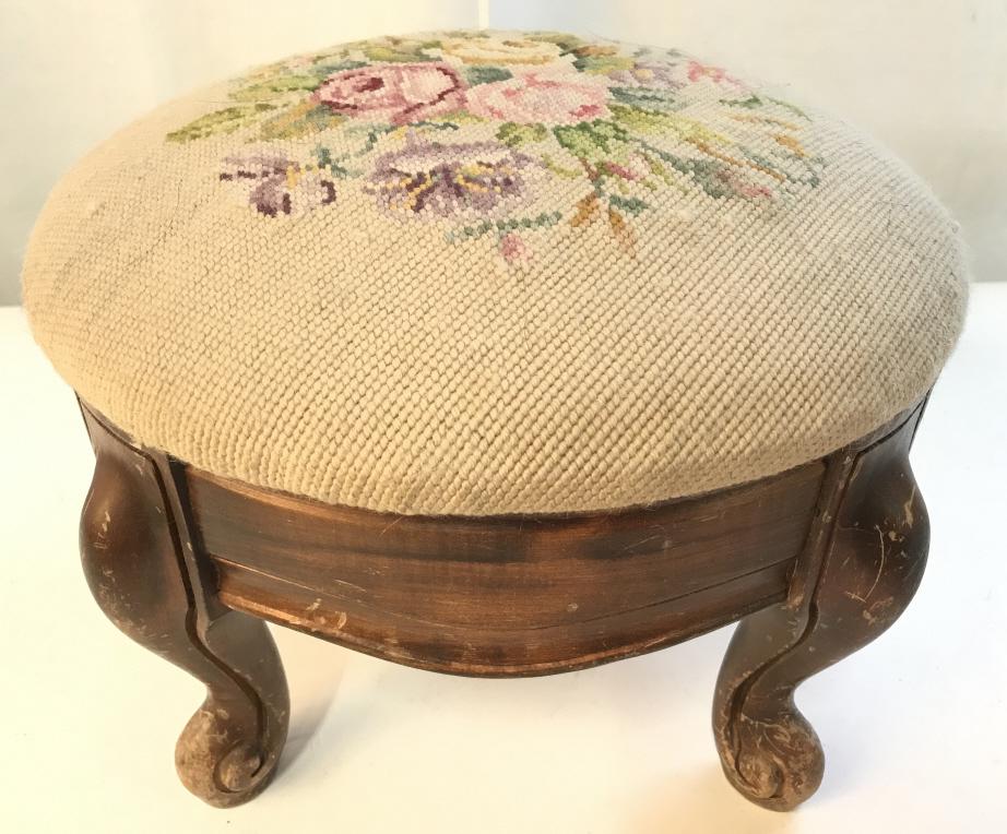 Vintage Needlepoint Upholstered Foot Stool: Footstool is upholstered with multi toned floral detailed Needlepoint upholstery. Piece is vintage possibly antique. Piece contains 4 carved wooden feet. Measures approx 14 inches wide 10 inches tall.