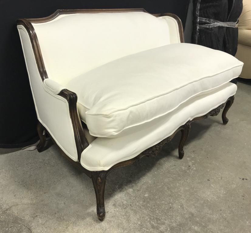 Cream Toned Love Seat W Carved Wooden Frame: Loveseat is cream toned. Contains brown toned carved wooden frame. Contains carved wooden feet. Measures approx 58 inches long 33 inches tall, 31 inches deep. Piece has some wear may need some restora