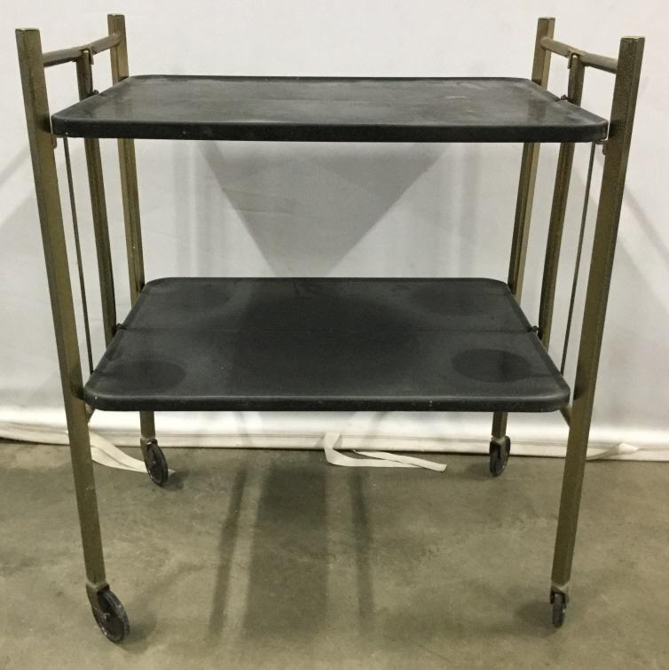Vintage Bi Level Metal Beverage Cart: Beverage cart is metal. Contains tones of black and gold. Piece has 4 wheel. Beverage cart, tea cart, bar cart, vintage bar cart. Both levels fold in center. Piece measures approx 26 inches long 32 in