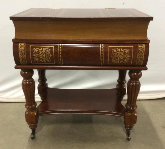 Stacked Wooden Book Side Table On Casters: Stacked Wooden Book Side Table On Casters, turned legs, gold toned painted design and top flips up to reveal storage, measures approximately 20 inches long x 13 inches wide x 22 inches tall, some nick