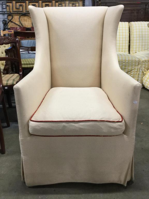 Vintage Skirted Wingback Armchair: Armchair has a winged backrest. Piece is cream toned. Seat cushion has red toned accent detail. Piece measures approx 43 inches tall 27 inches wide 32 inches deep. arm chair, home accent and furnishin