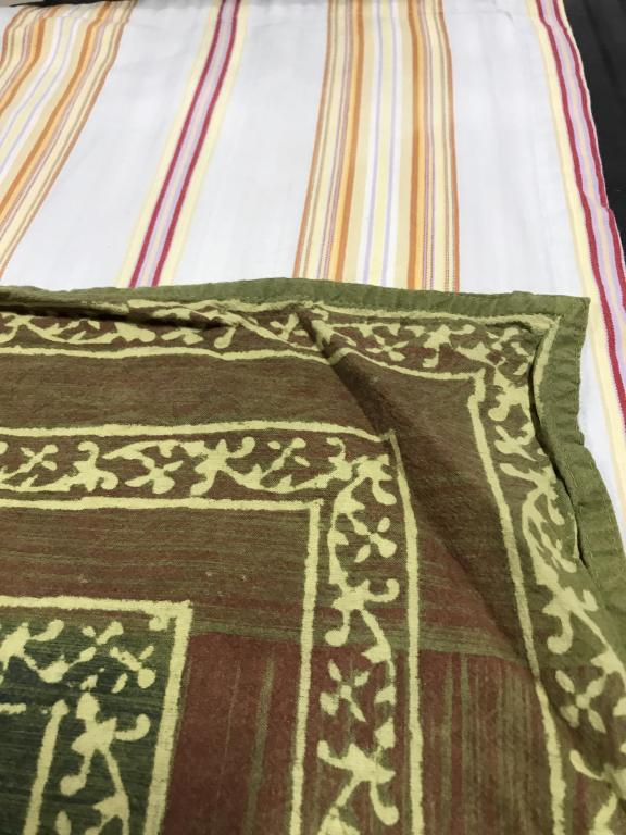 Lot 2 Vintage Cotton Tablecloths: Cloth 1 is white with orange, red, yellow, violet thin stripe pattern. Measures 58 x 54.5 in. A couple of blemishes. Cloth 2 is similar to a green batik. Has stripe column pattern around edges with ce