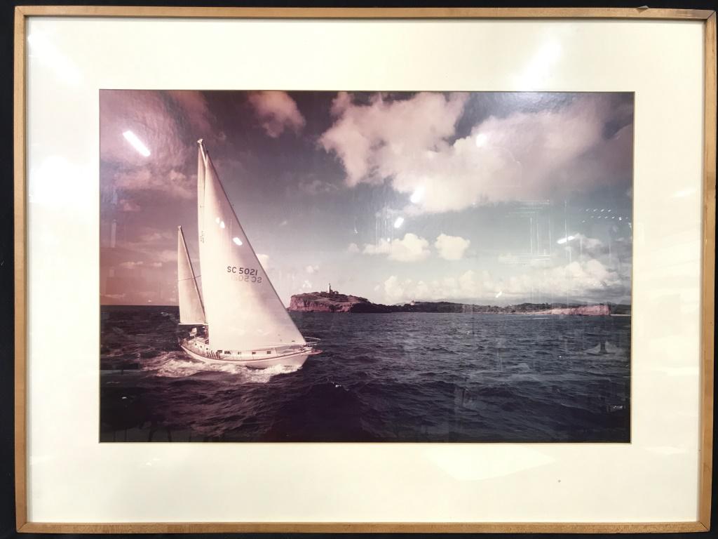 Framed Nautical Photographic Print: Photographic print depicts boat sailing and Land with a lighthouse in the background on a partly cloudy day. Piece is professionally framed & matted with beige toned frame. Piece measures approx 38 in