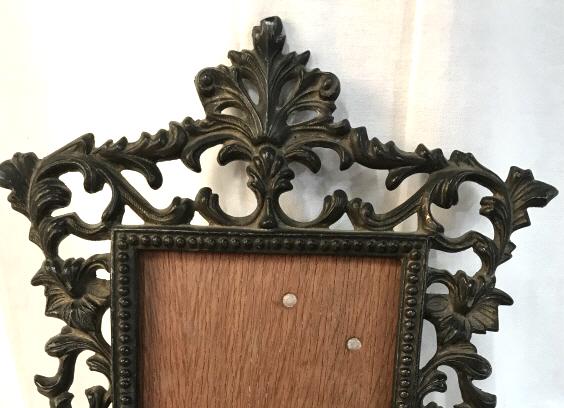 Lot 2 Bronze Vintage Picture Frames: One Art Deco frame, bronze, ‘sun’ face & shooting Art Deco sun rays ,swirling organic shapes. Glass cut to shape of frame. Hanging wire in back. Must screw off backing to slip in art/ photo. 9 x 1