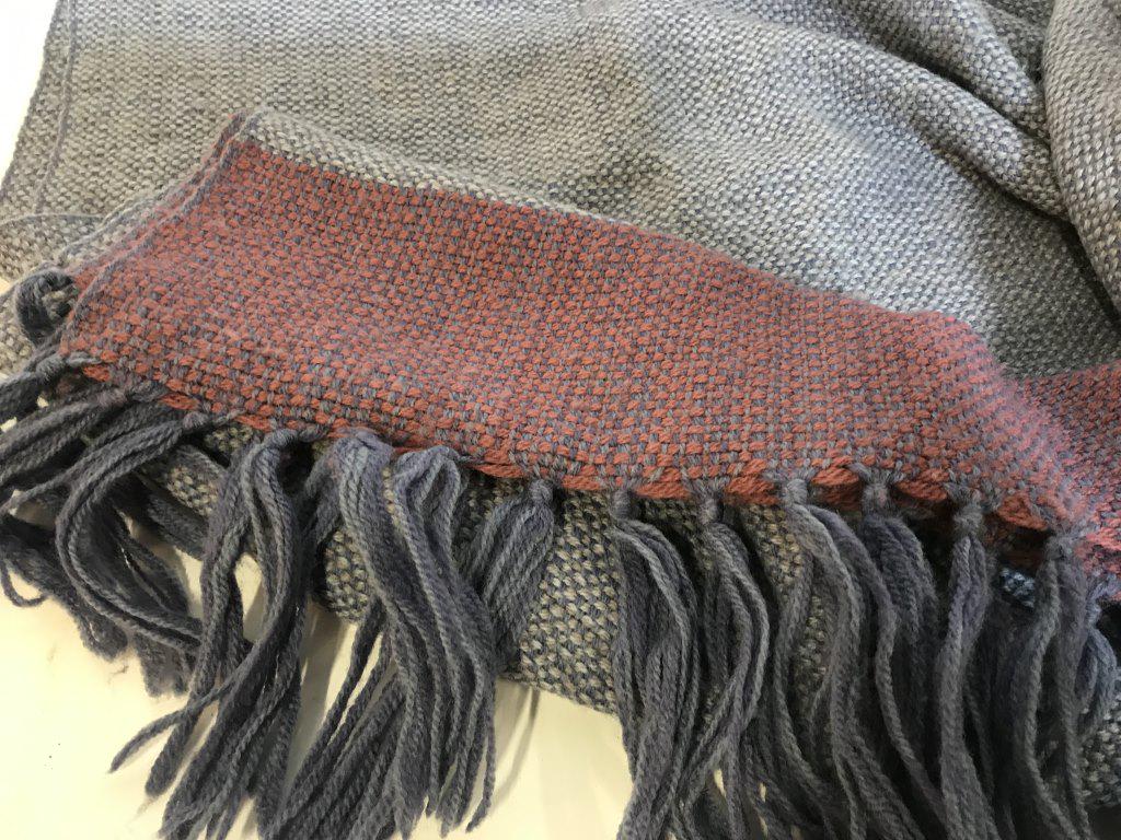 Hand Knitted Wool Throw Blanket, The Three Weavers: Long yarn tassel edges, knitted with blue and dark pink wool yarn. Some pilling. spot discoloration. Warm, soft. Approx 53 x 34.5 in., tassels xtra 5 in. label reads ‘ 100% Virgin Wool, The Three We