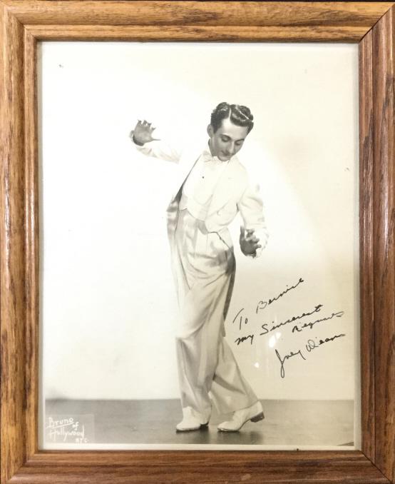 Signed Photographic Print Of Man In a White Suit: Piece is professionally framed with wooden frame. Piece depicts a male figure dancing in a white toned suit. Piece appears to be signed on lower right area. Lower left area reads BRUNO OF HOLLYWOOD. P