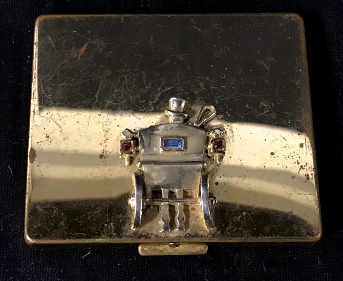 Vintage Flato Gold Toned Compact mirror: Rectangular shaped compact mirror in gold tone. Measures approximately 2.5 by 2.25 inches. dimensional image of the back of a carriage, Colored gems on carriage. Mirror, compact mirror, vintage compac