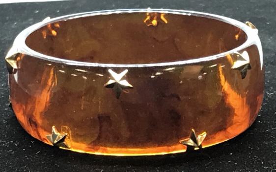 Star Studded Bakelite Bangle: Warm Amber color Bakelite Bangel with gold tone star tacks alternating along edges. 1 in wide material. Opening diameter 2.5 in. Overall size 2.75 in. diameter. Bakelight was developed in Yonkers, Ny 