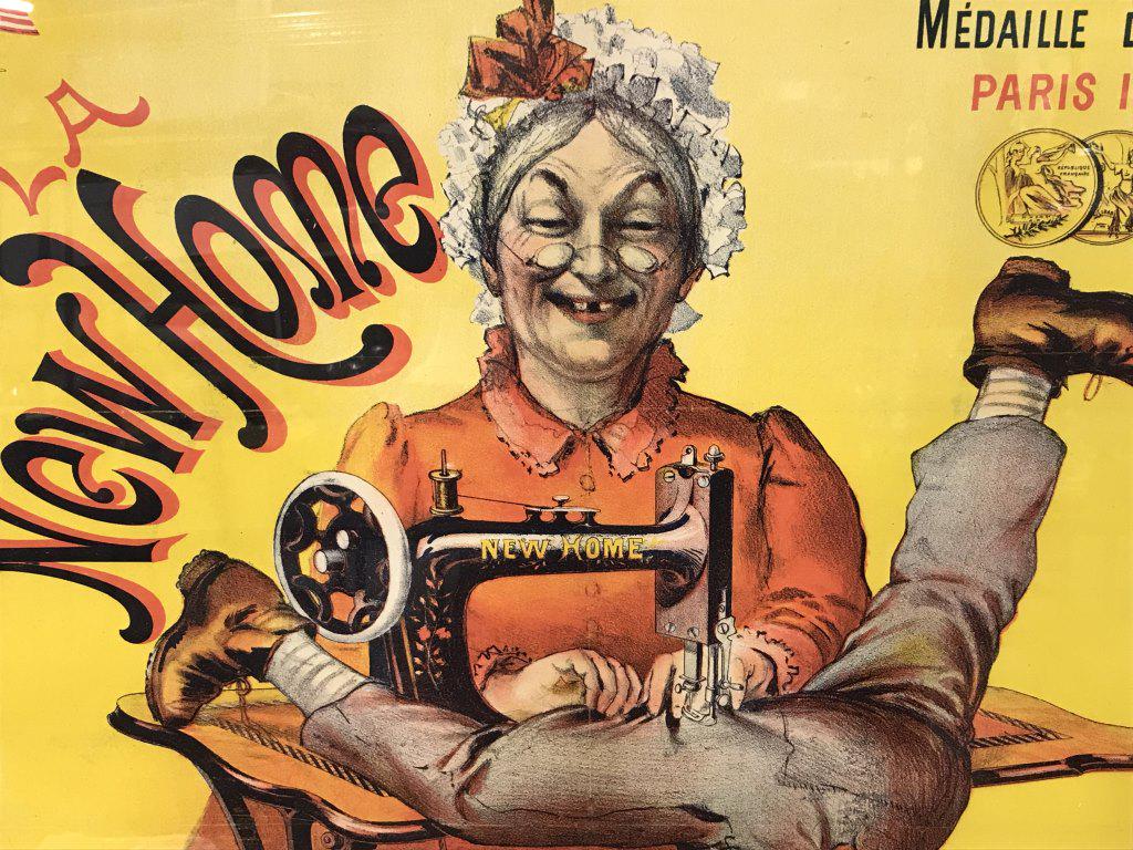 Vintage Framed French Poster, ‘La New Home’: Vintage, possibly antique, framed poster titled ‘La New Home,’ depicting an elderly woman sewing into the pants of a young boy as he dangled from the sewing machine. Type in upper right corner rea