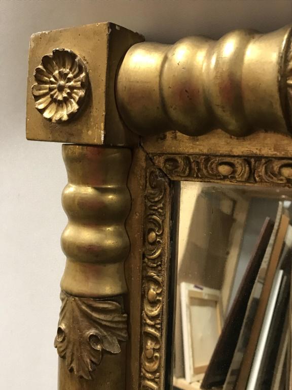 Antique Gold Tone American Empire Mirror: Antique American Empire style mirror with corner details. Mirror is set in gold tone wood frame. Measures approx 20.25 inches in height by 29.5 inches in width. Frame of mirror has surface wear, inclu