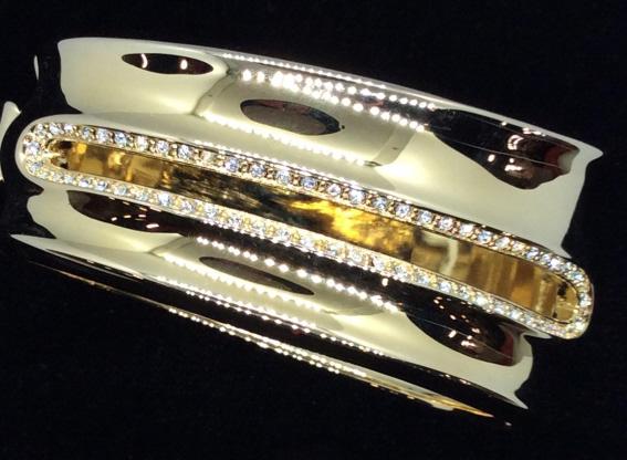 Signed Adrienne Vittadini Crystal Hinge Cuff: Smooth gold tone metal with center line insert design of brilliant clear rhinestones, Push open clasp that snaps. Signed ‘Adrienne Vittadini ‘ app 3 x 2.5 in. Comes in grey gift pouch. Collectible