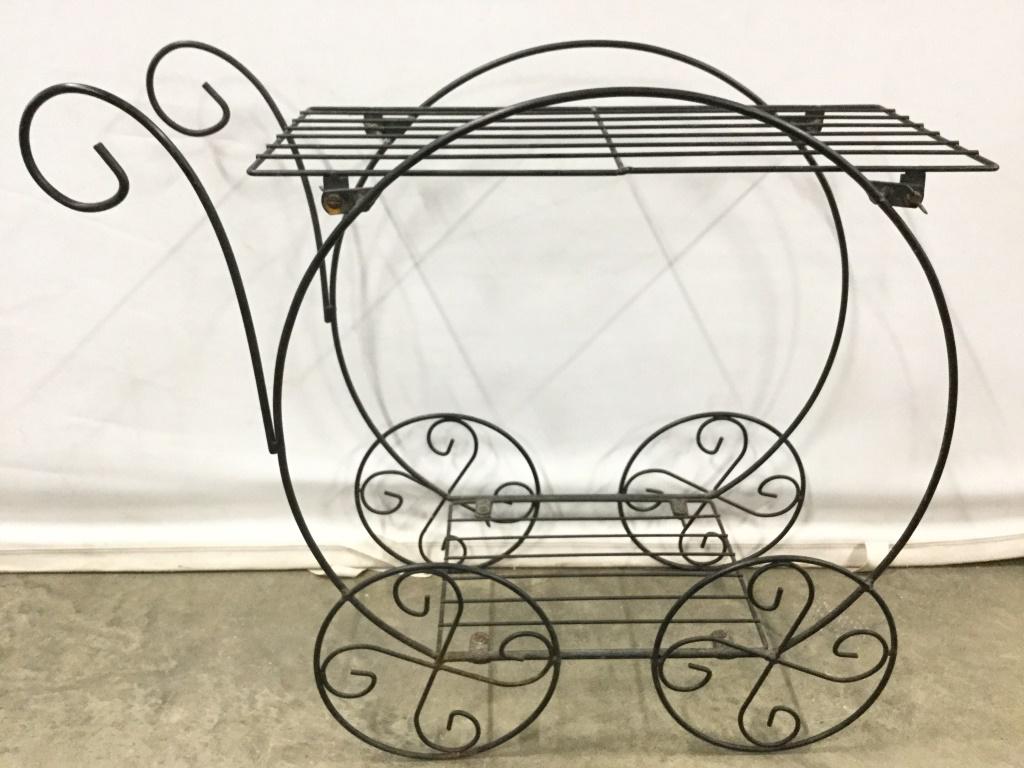 Black Toned Metal Cart Planter Stand: Planter stand is black toned and metal. Piece has cart like shape. Planter stand has 2 levels. Piece measures approx 25 inches long 23 inches tall. bar cart, drinks cart, plant stand, garden accessory
