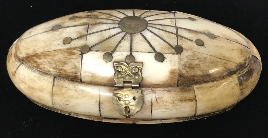 Natural Bone & Brass Keepsake Box: Oblong shape carved and smoothed bone box with inlaid brass decor detail in shape of a sun dial. Brass hinged and clasps. Interior lined with purple velvet. 6.5 x 3.5 x 1 3/4 in. Trinket box, carved b