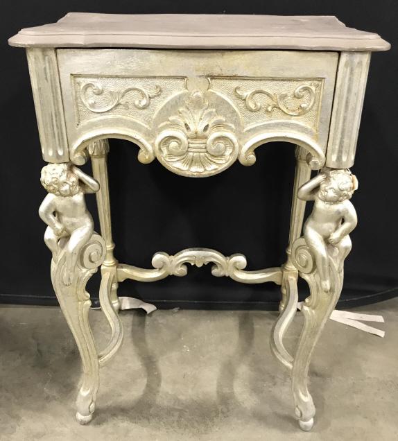Antique Carved Wooden Cherub Leg Side Table: Table has carved wooden cherub legs. Piece has 1 drawer. Tabletop is slate toned. Piece appears to be painted with a light gold tone. Piece has carved floral detail on sides. Piece measures approx 30