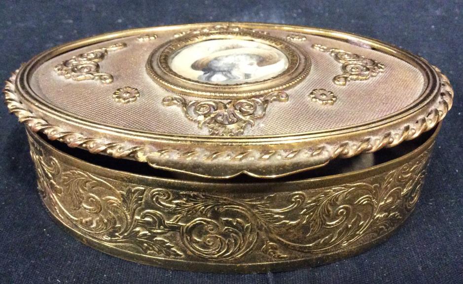 Vintage Gold Toned French Metal Trinket Box: Trinket Box is gold toned and metal. Piece is oval & contains ornate detail. Center has depiction of female figure wearing a hat. Piece is vintage Possibly antique. Piece measures approx 4.5 inches lo