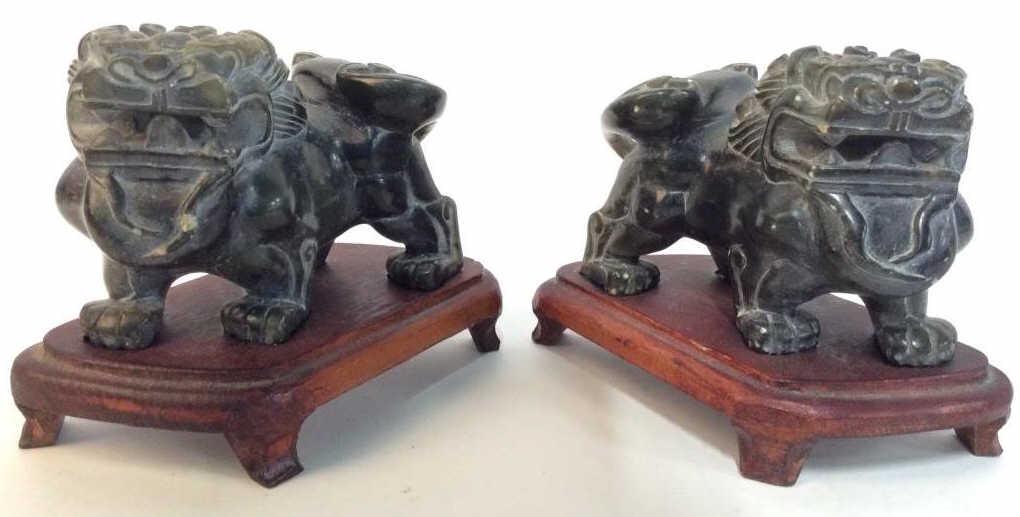 Pair Carved Stone Foo Dogs W Stands: Lot includes 2 foo dogs. Each appears to be carved stone. Each includes petite wooden stand. Each piece on stand measures approx 4.5 inches long 3.5 inches tall and wide. Each piece has some minor chi