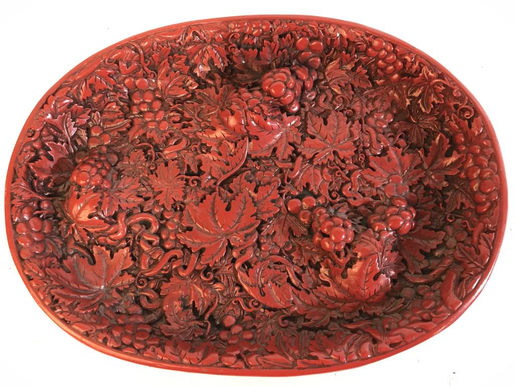 Signed Oval Shaped Carved Cinnabar plaque: Cinnabar dish is red toned. Contains intricately carved floral vine and leaf detail. Piece is signed on underside with Asian characters. Piece measures approx 9.5 inches long 7 inches deep. dish, trin