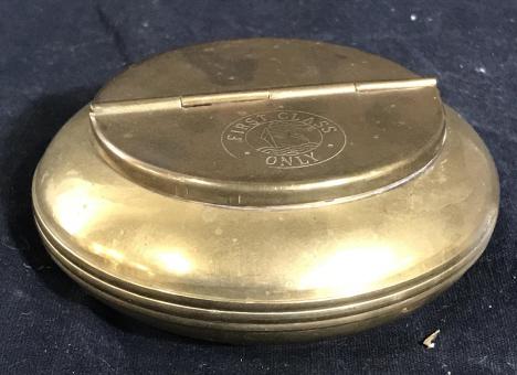 Brass Yacht Ashtray, Vintage: Ashtray Vessel with hinged lid. Cigarette indentations to rest cigarette and have ashes fall into vessel. Exterior etched with boat that reads ‘ First Class Only’. App 4.5 in. diameter. App 2.5 by