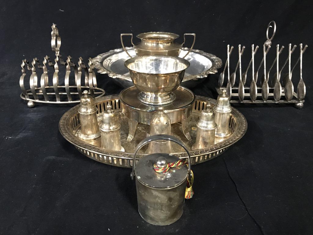 Lot 12 Silver Plated Tabletop Accessories: Lot includes 2 toast Holders, 1 oval shaped tray, 1 circular shaped tray with ornate detail around edges, 5 salt & Pepper Shakers, 1 candle, 1 trophy shaped vessel, & 1 Footed Stand. Largest tray meas