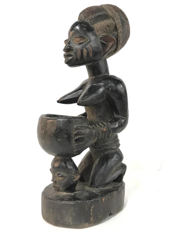 African Art Yoruba Tribe Carved Figural Sculpture: African art carved wooden sculpture from the Yoruba people in Nigeria. Sculpture depicts kneeling female figure holding bowl with figurehead base. Sculpture measures approx 20.75 inches in height by 6