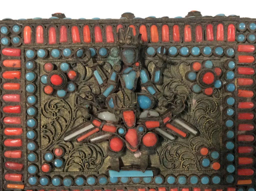 Tibetan Brass Filigree & Beaded Hinged Trinket Box: Tibetan Brass Filigree Hinged Trinket Box, with turquoise-style and coral-Style bead inserts throughout. Lid depicts two god-like figures. Measures approx 1.5 inches in height by 4 inches in width by 