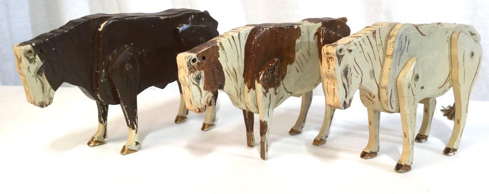 Set 3 Folk Art Wooden Cow Figurals: folk art carved cows with moveable features. Set of 3 decorative wooden cows, the tails are crafted from twine or rope. The pieces measure approx 6 inches H, 2.12 inches wide, and 9.5 inches long. The